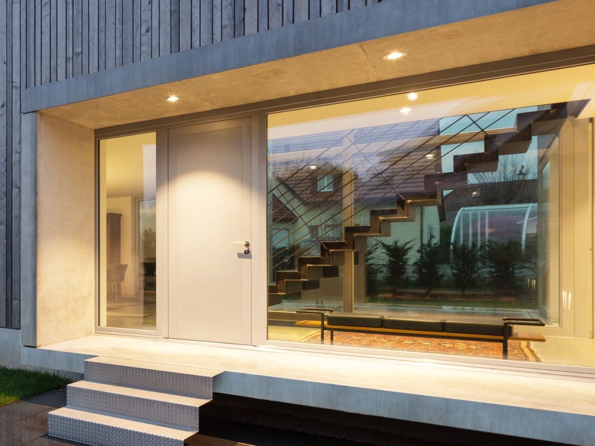 A modern home with a light grey entrance door and full height glazing at dusk