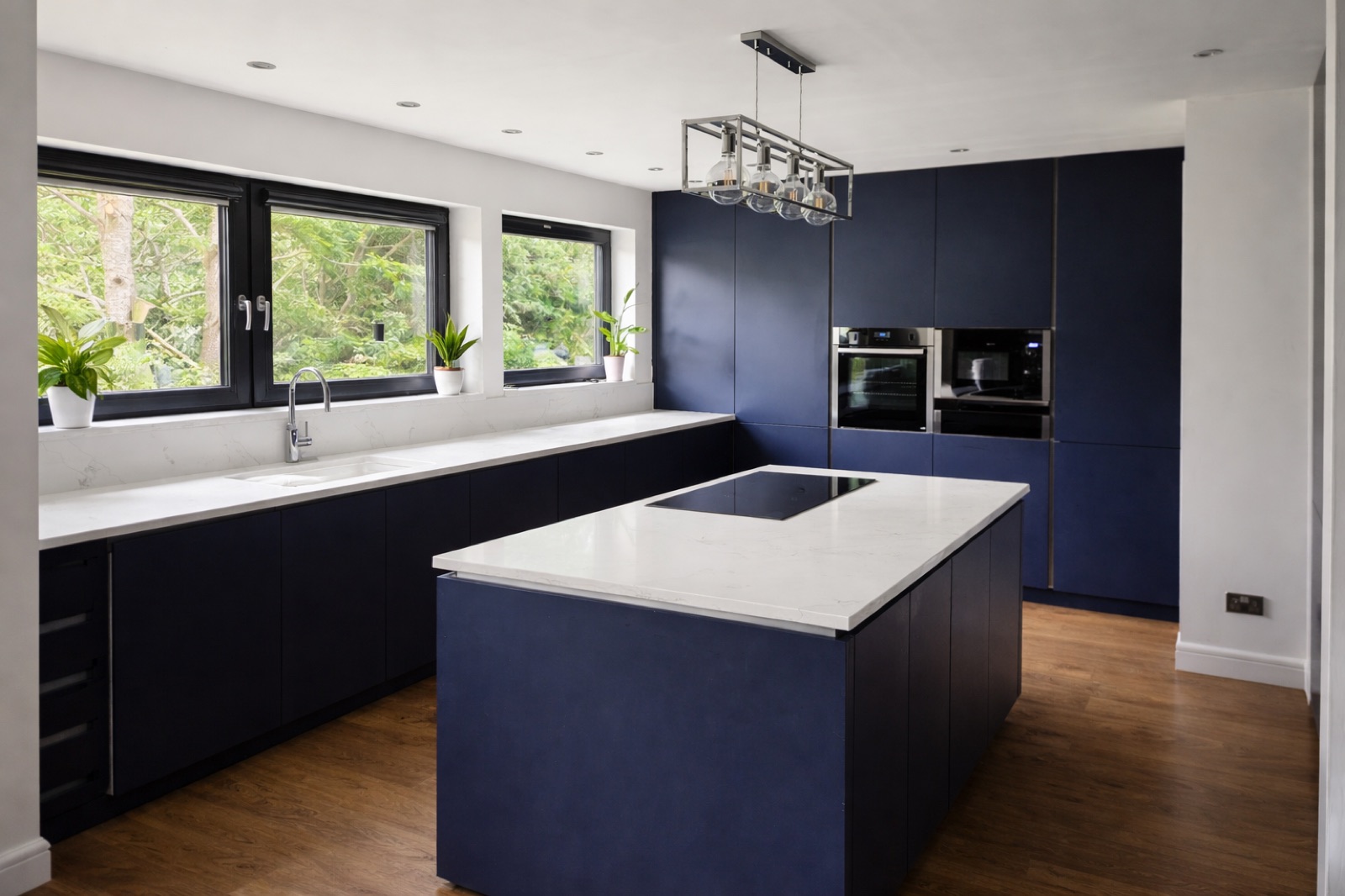 A navy kitchen with black framed windows overlooking greenery